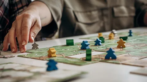 Close-up of a person's hand moving a pawn on a board game.