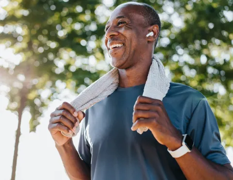 A smiling male wearing ear buds holding a towel that he is using for his workout.