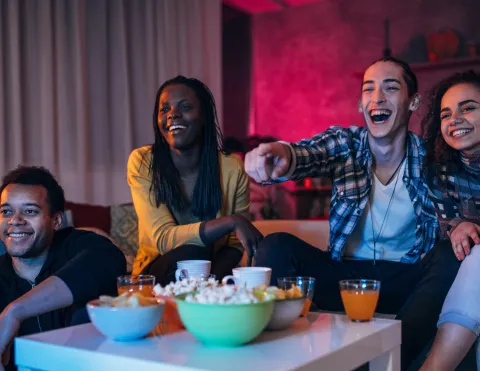 Four People Enjoying Themselves, Laughing with Snacks on the Table in Front of Them.