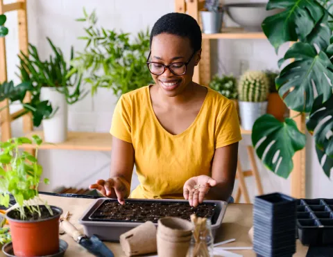 A woman surrounded by plants, planting a seed.