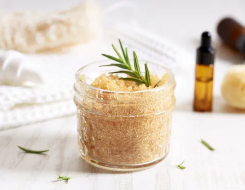 A container of Sugar Scrub with essential oil bottles next to it.