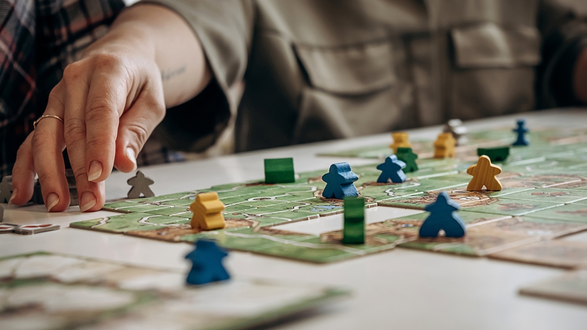 Close-up of a person's hand moving a pawn on a board game.