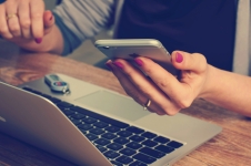 Hand holding an iPhone and sitting in front of an open laptop