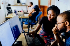 Two people staring at a computer screen and one person helping the other